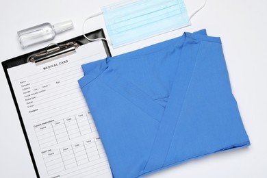 Photo of Medical uniform, face mask and clipboard on white background, flat lay