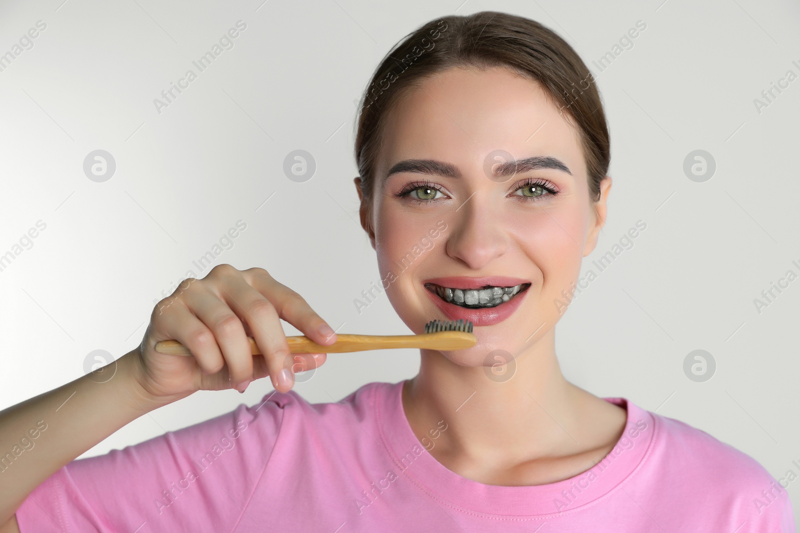 Photo of Young woman brushing teeth with charcoal toothpaste on light background