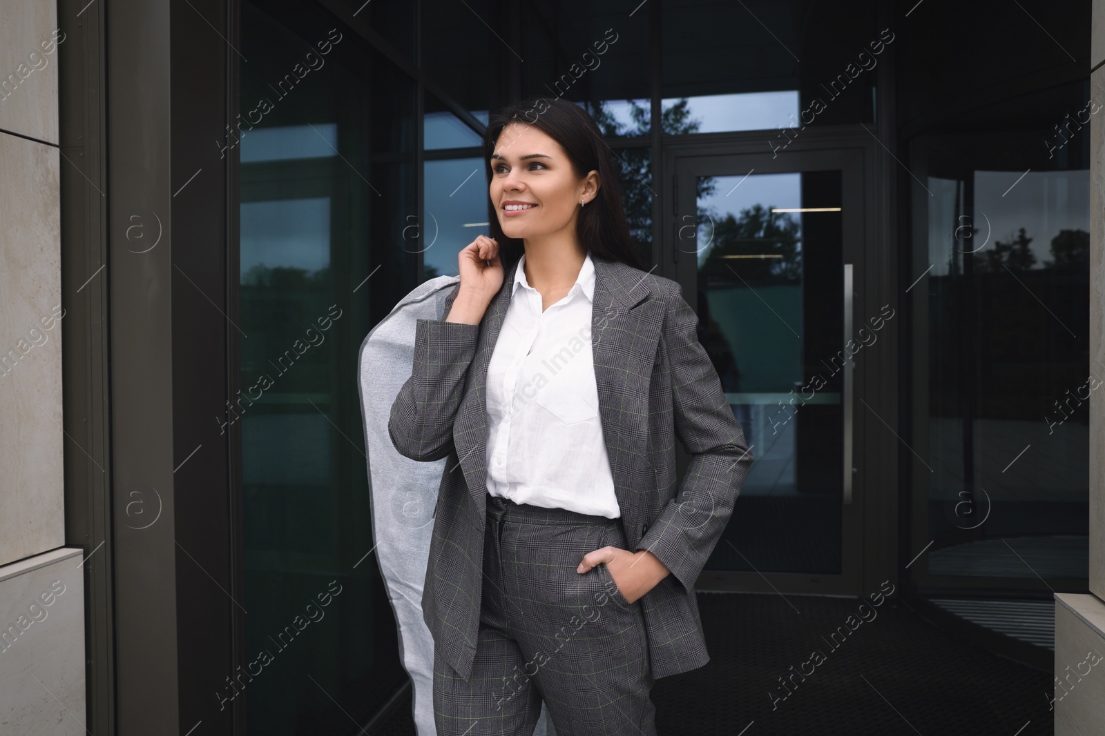 Photo of Attractive happy businesswoman holding garment cover with clothes outdoors. Dry cleaning service