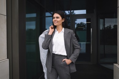 Photo of Attractive happy businesswoman holding garment cover with clothes outdoors. Dry cleaning service