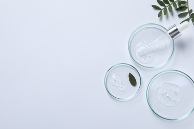 Petri dishes with samples of cosmetic oil, pipette and green leaves on white background, flat lay. Space for text