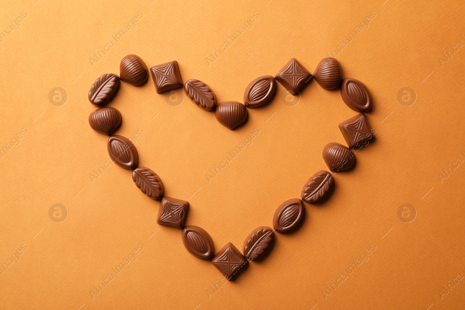 Photo of Heart made with delicious chocolate candies on brown background, top view