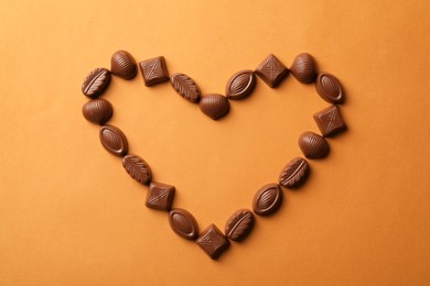 Heart made with delicious chocolate candies on brown background, top view