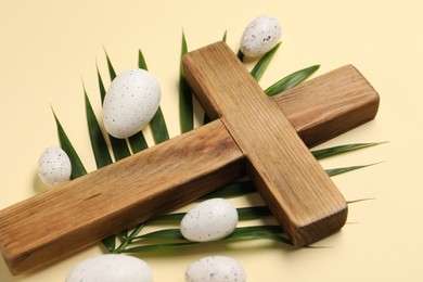 Wooden cross, painted Easter eggs and palm leaf on beige background