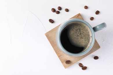 Photo of Delicious coffee in cup and beans on white textured table, top view. Space for text