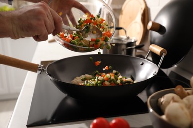 Photo of Man pouring mix of fresh vegetables into frying pan, closeup