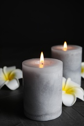 Photo of Burning candles and plumeria flowers on dark grey table against black background, space for text