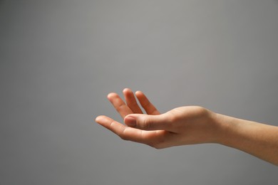 Woman holding something in hand on grey background, closeup. Space for text