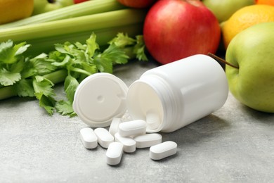 Photo of Dietary supplements. Overturned bottle and pills near food products on grey textured table