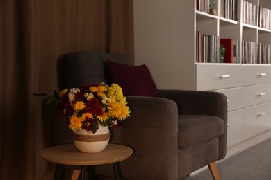 Photo of Comfortable armchair and vase with beautiful flowers in cozy home library interior