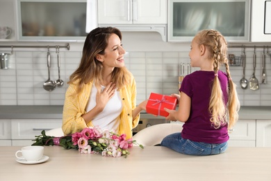 Photo of Little daughter congratulating her mom in kitchen. Happy Mother's Day