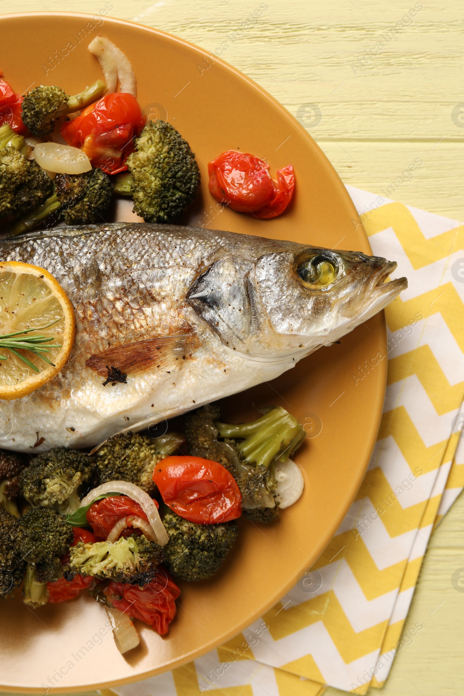 Photo of Delicious baked fish and vegetables on yellow wooden table, top view