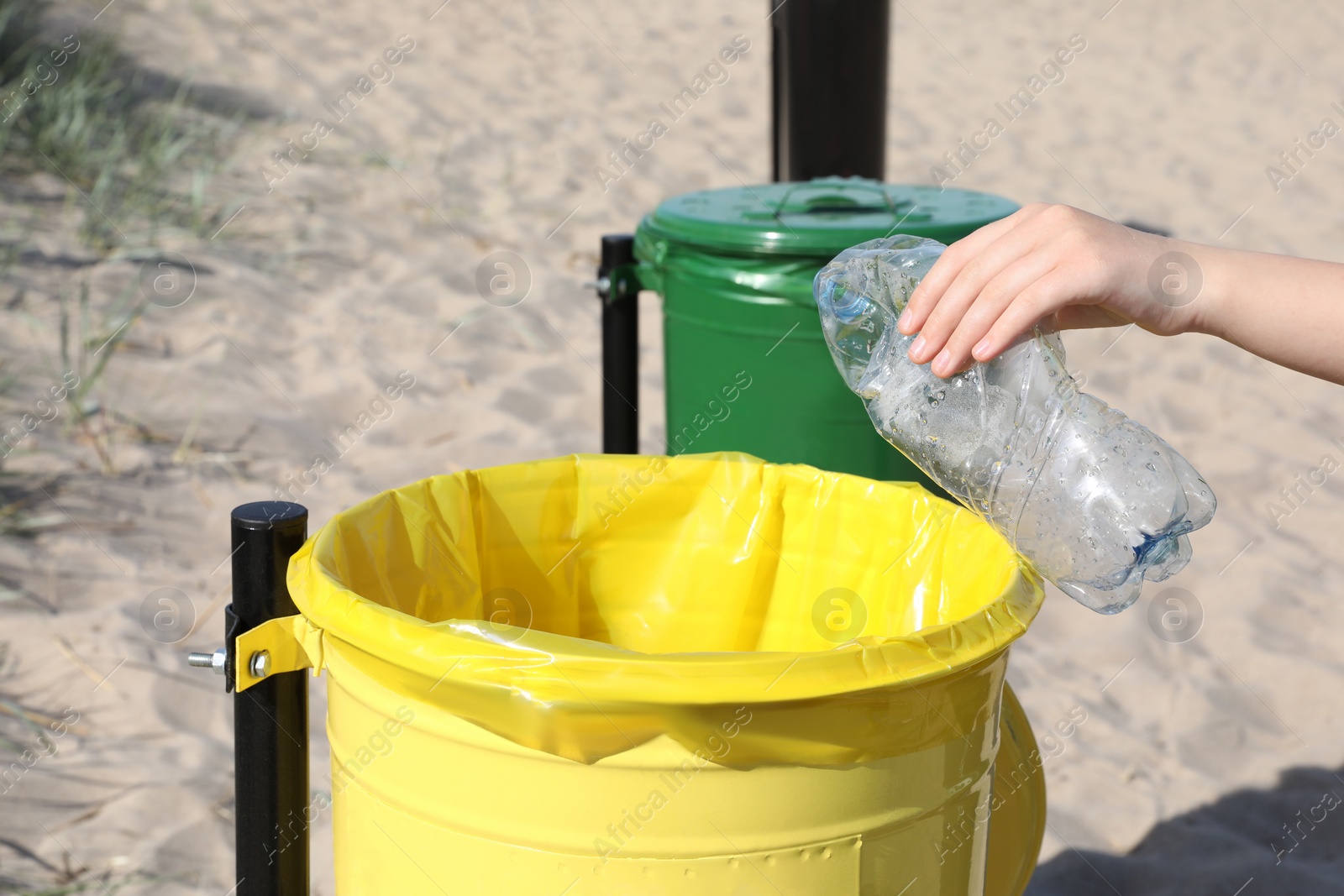 Photo of Woman throwing plastic bottle in yellow bin on beach, closeup. Recycling concept