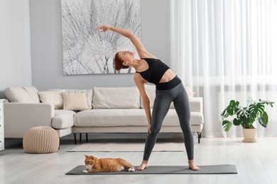 Photo of Beautiful woman with cute red cat practicing yoga on mat at home