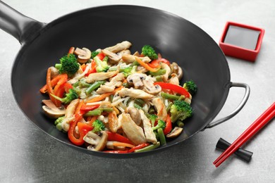 Photo of Stir fried noodles with mushrooms, chicken and vegetables in wok on light grey table