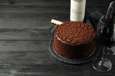 Photo of Delicious chocolate truffle cake, red wine and corkscrew on black wooden table, space for text