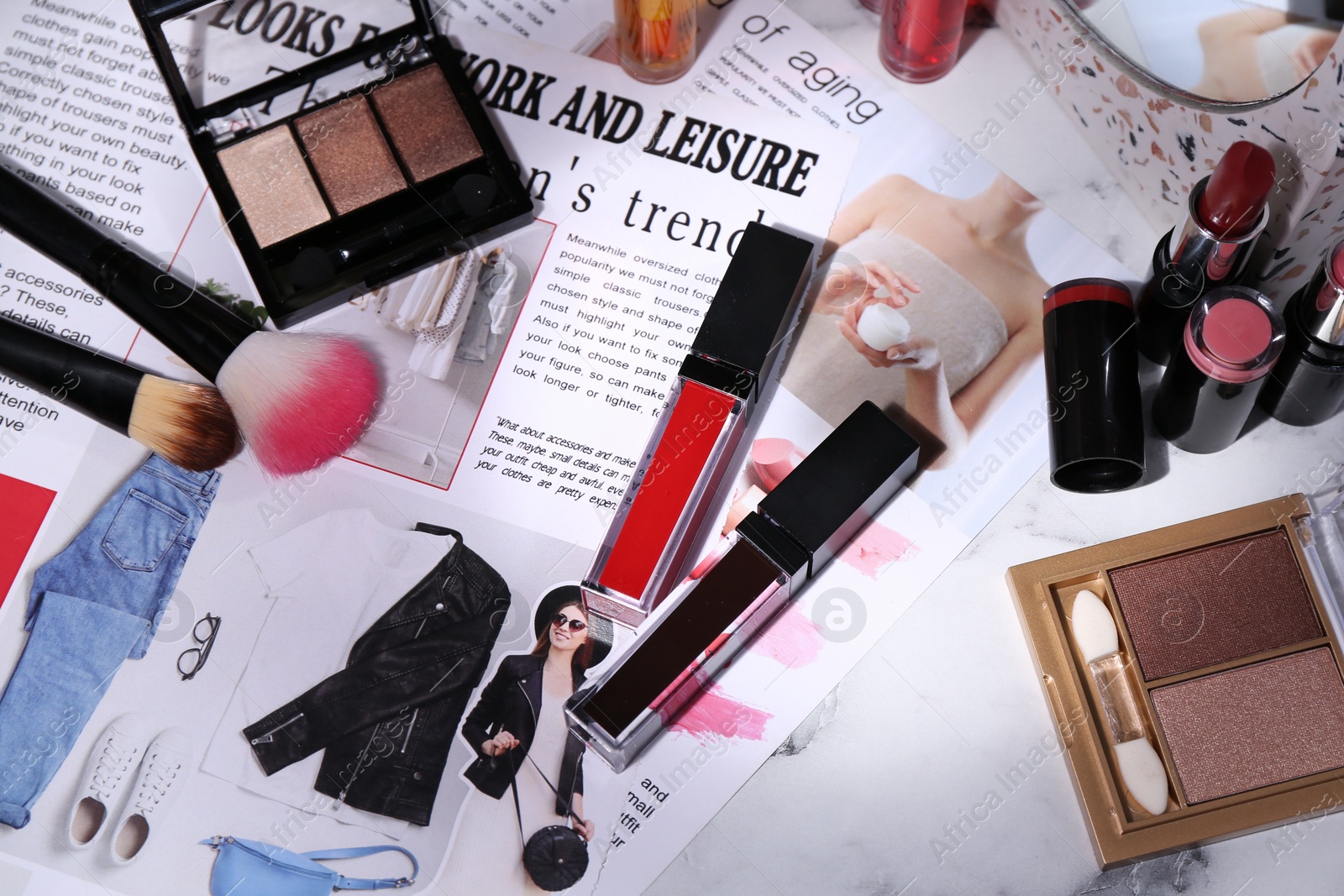 Photo of Bright lip glosses among different cosmetic products and fashion magazine on table