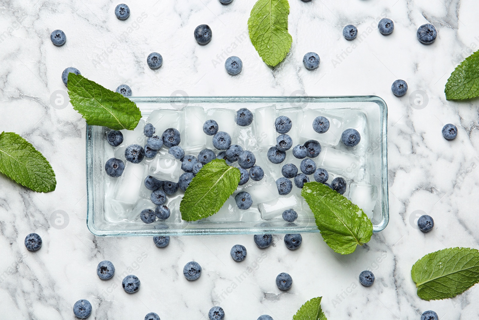 Photo of Flat lay composition with juicy blueberries, green leaves and ice on marble table