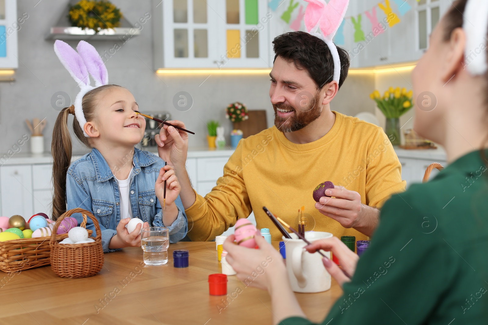 Photo of Happy family having fun while painting Easter eggs at table in kitchen