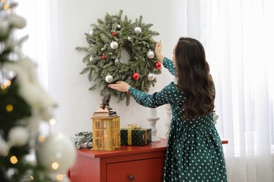 Photo of Young woman decorating Christmas wreath at home