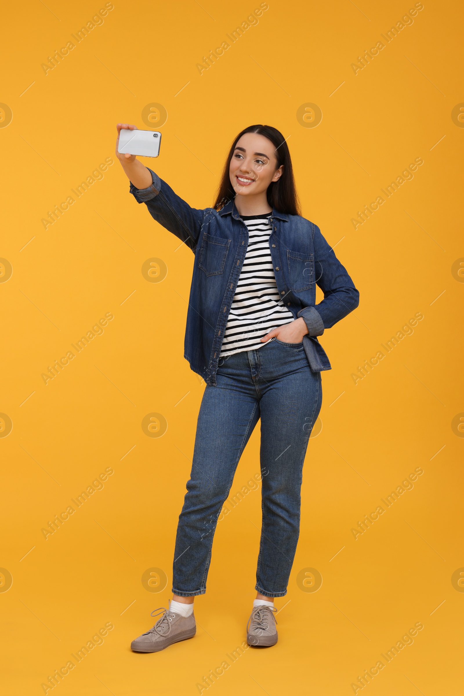 Photo of Smiling young woman taking selfie with smartphone on yellow background