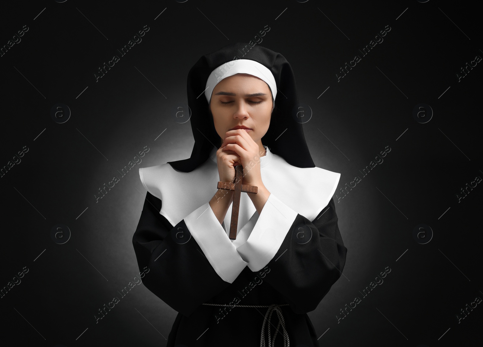 Photo of Nun with clasped hands praying to God on black background