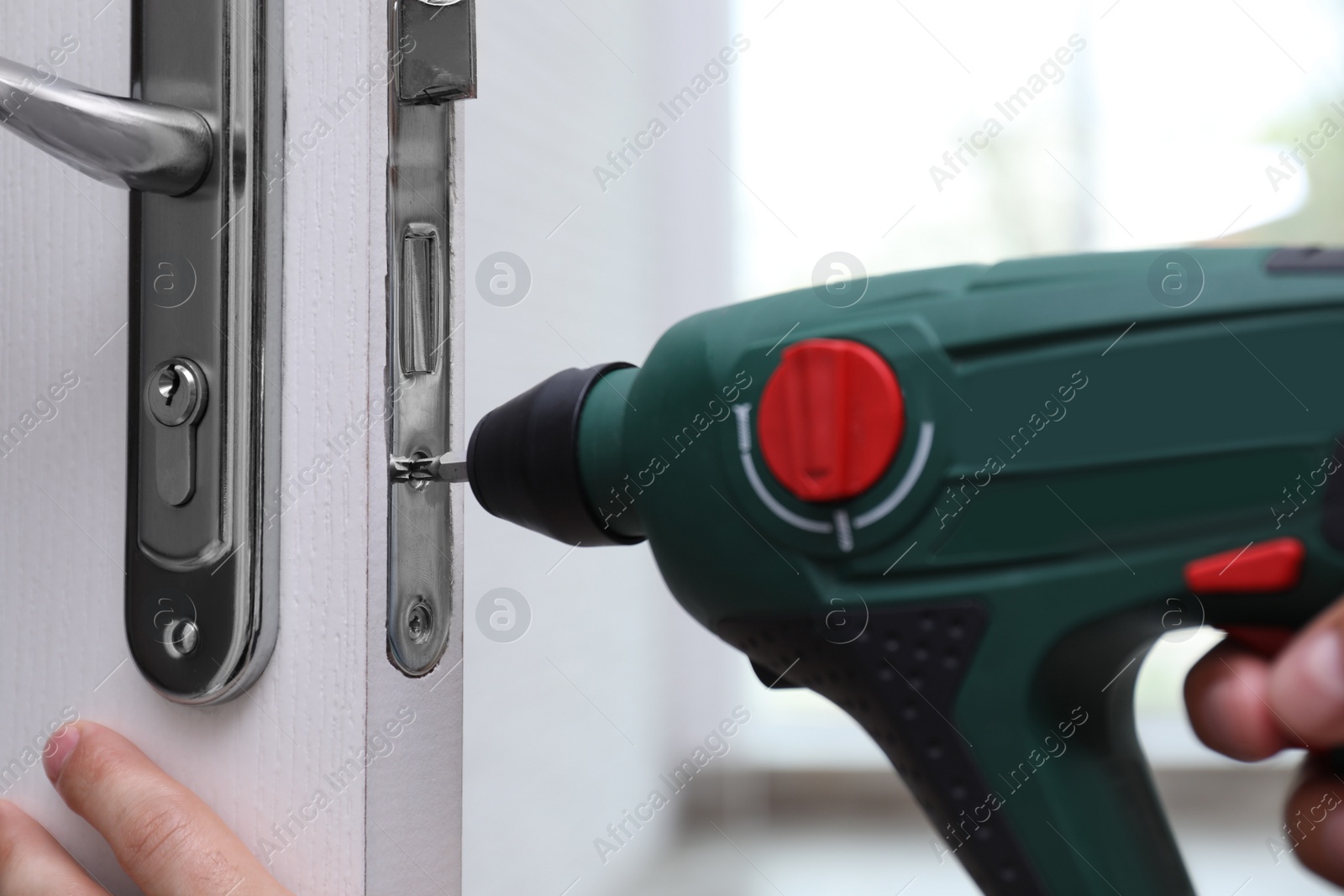 Photo of Handyman with screw gun repairing door lock indoors, closeup