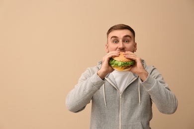 Photo of Young man eating tasty burger on color background. Space for text