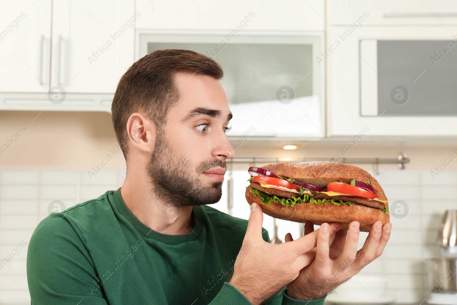 Photo of Young hungry man eating tasty sandwich in kitchen