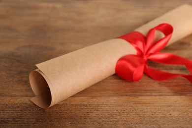 Rolled student's diploma with red ribbon on wooden table, closeup