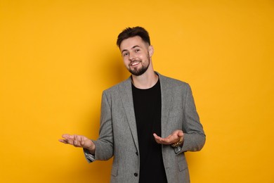 Photo of Handsome man in stylish grey jacket gesturing on yellow background