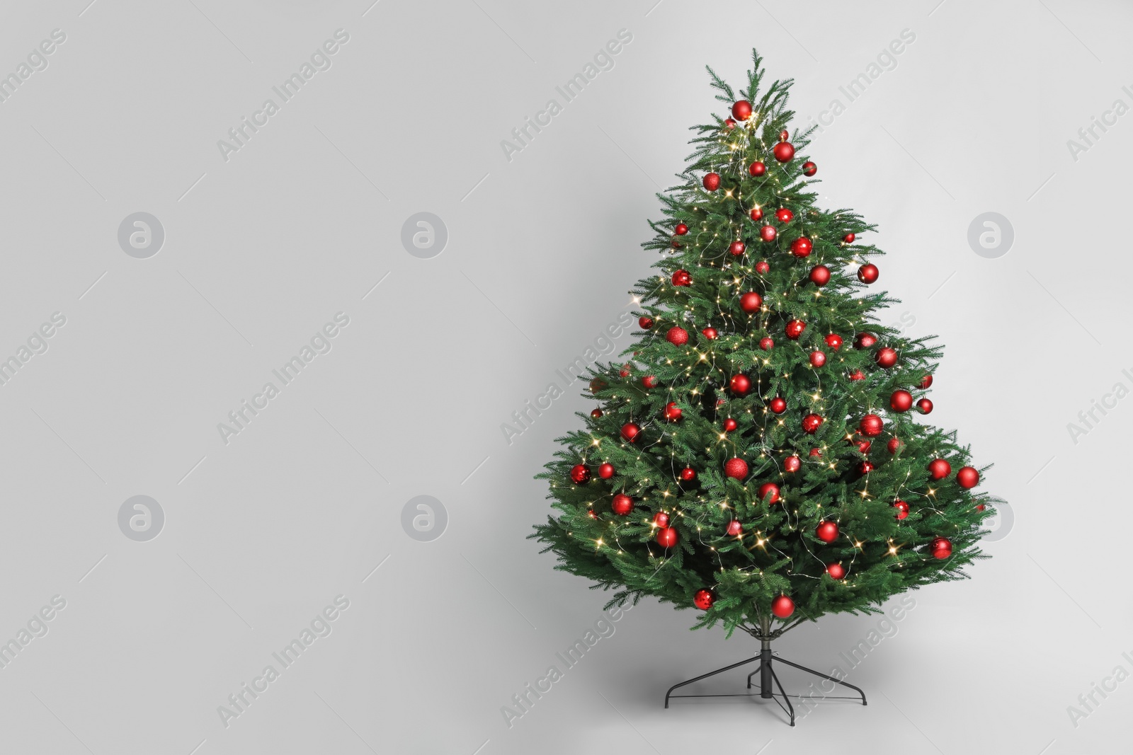 Photo of Beautiful Christmas tree with red baubles and fairy lights on white background