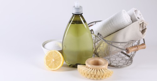 Bottle of cleaning product, brush, rags and lemon on light background