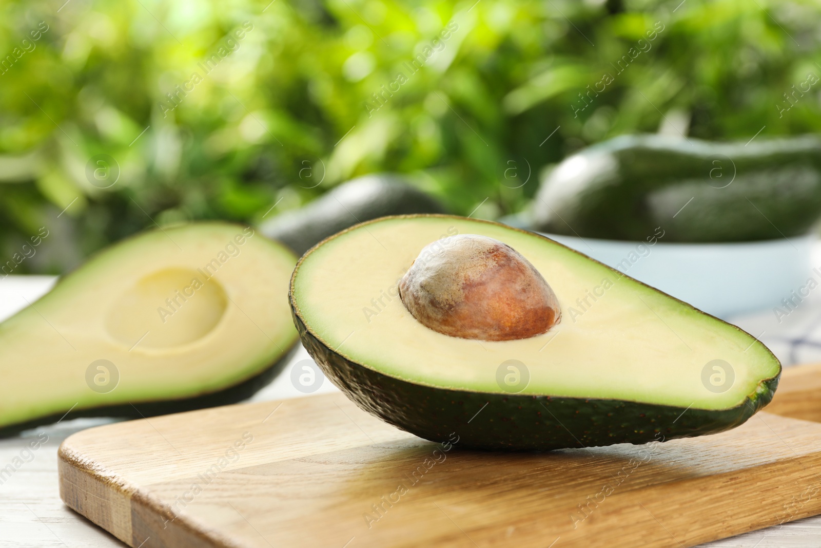 Photo of Half of delicious ripe avocado on wooden board against blurred background