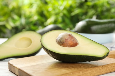 Photo of Half of delicious ripe avocado on wooden board against blurred background