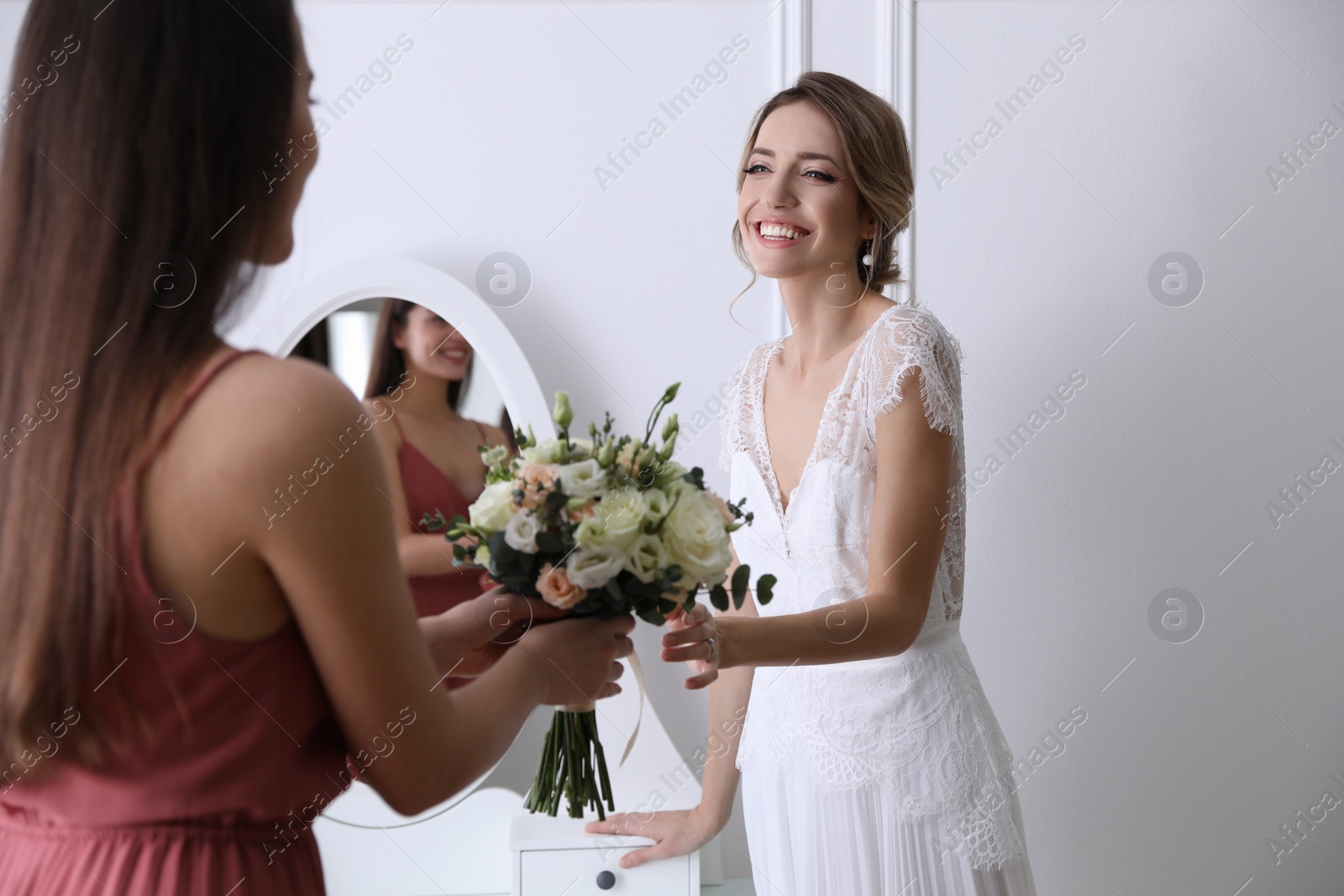 Photo of Bridesmaid giving bouquet to beautiful woman in wedding dress indoors