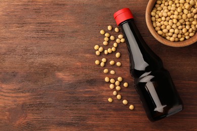 Photo of Bottle of soy sauce and soybeans on wooden table, flat lay. Space for text