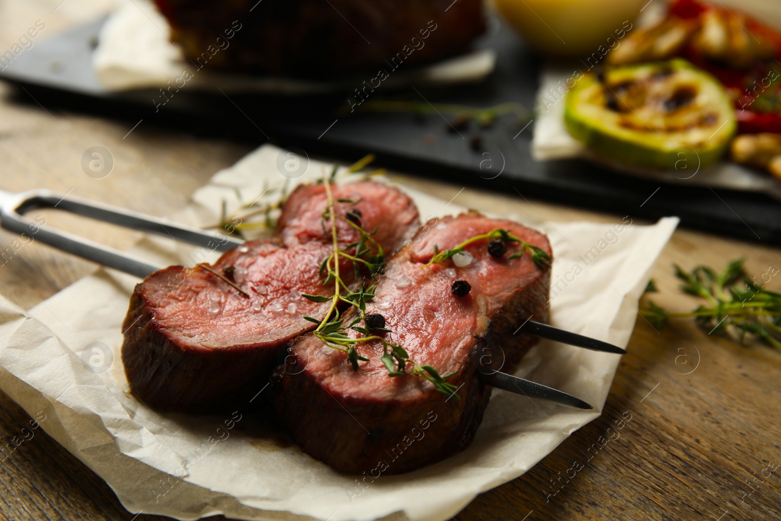 Photo of Fork with slices of grilled meat on wooden table