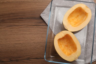 Photo of Raw spaghetti squash halves in glass baking dish and napkin on wooden table, top view. Space for text