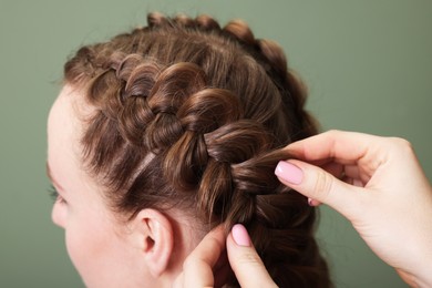 Professional stylist braiding woman's hair on olive background, closeup