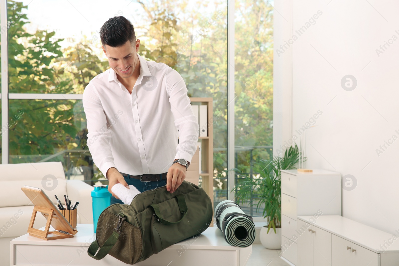 Photo of Businessman packing sports stuff for training into bag in office