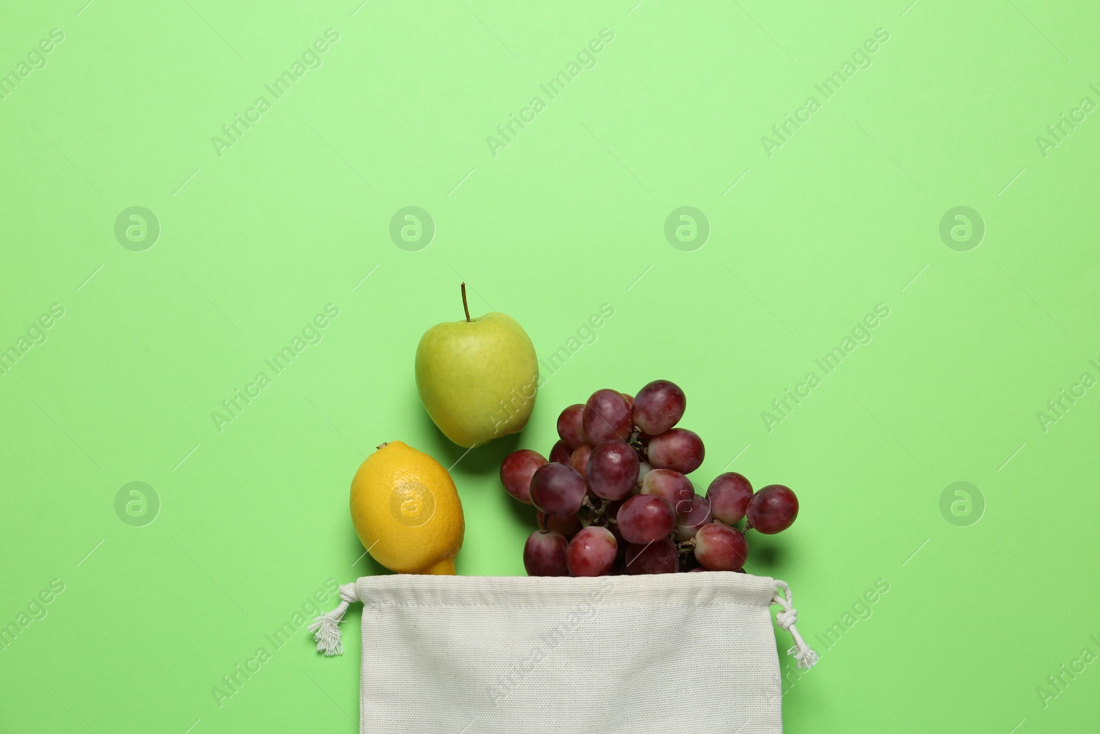 Photo of Cotton bag with juicy fruits on green background, flat lay