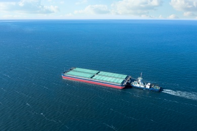 Image of Tugboat pulling barge with cargo by water,  aerial view
