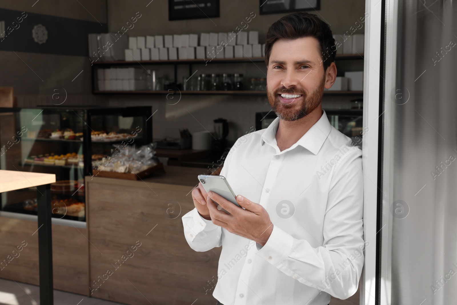 Photo of Happy business owner with smartphone in bakery shop. Space for text