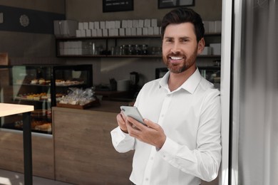 Photo of Happy business owner with smartphone in bakery shop. Space for text