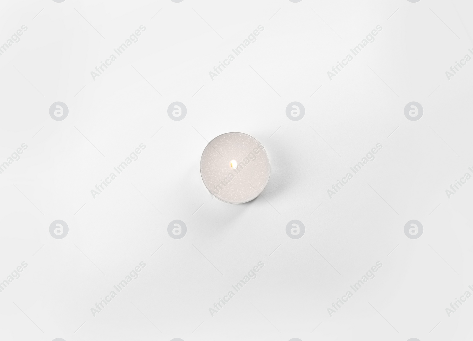 Photo of Burning tea candle isolated on white, top view