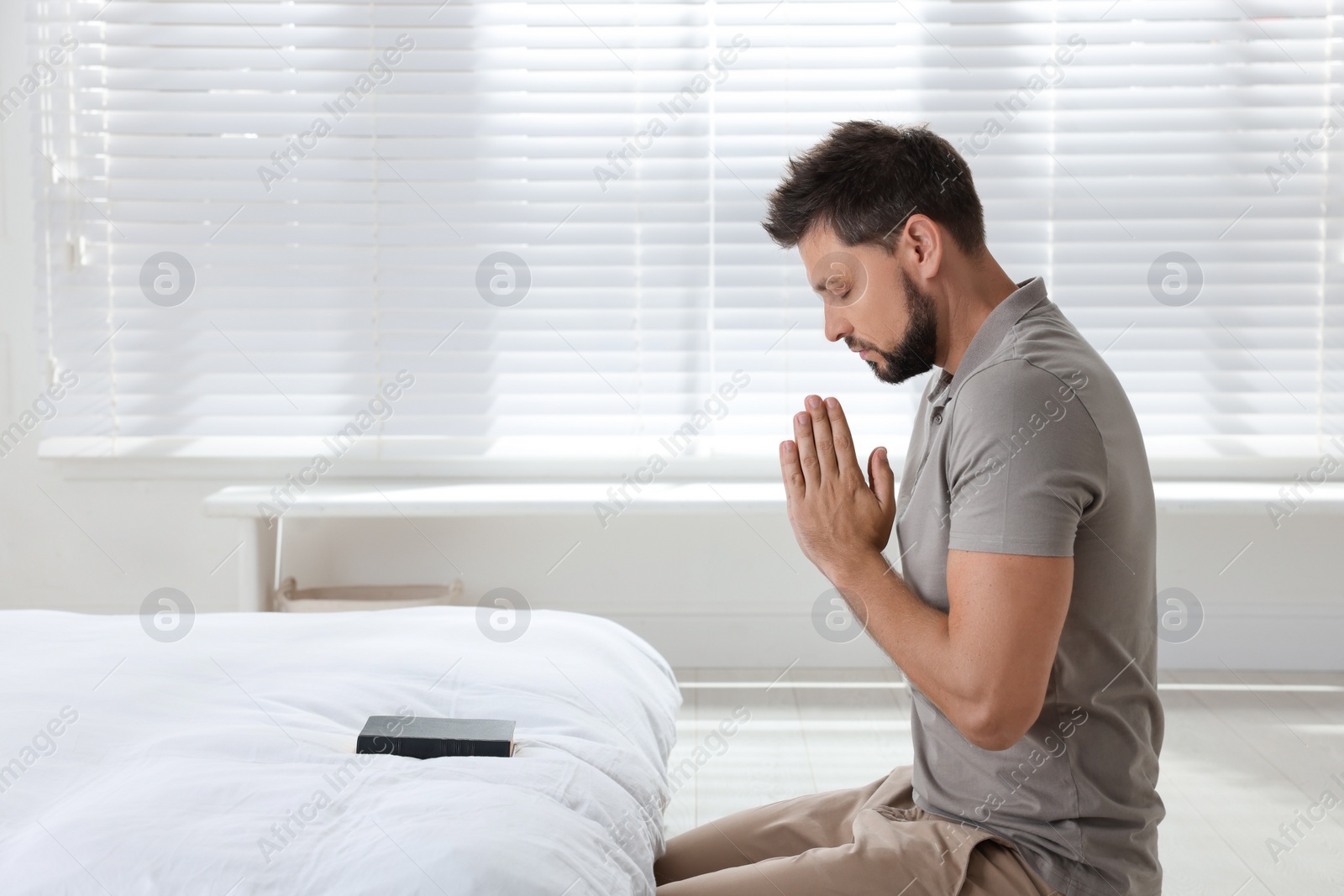 Photo of Religious man with Bible praying in bedroom