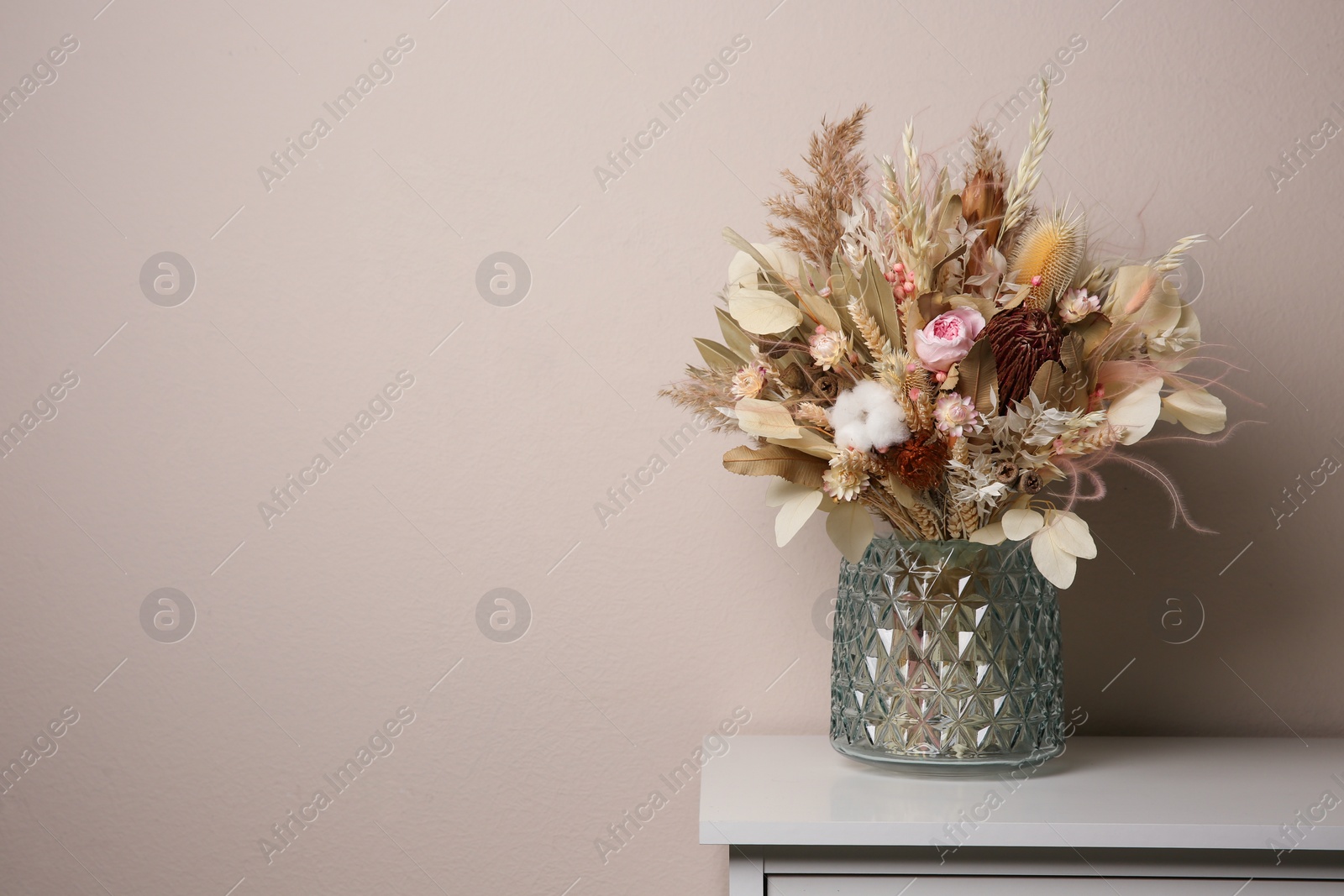Photo of Beautiful dried flower bouquet in glass vase on white table near light grey wall. Space for text