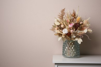 Photo of Beautiful dried flower bouquet in glass vase on white table near light grey wall. Space for text