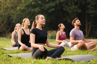 Photo of Group of people practicing yoga on mats outdoors. Lotus pose